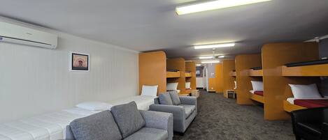 A room with bunk beds, a sofa, and a bed. There is a ceiling fan and an air conditioning unit.
