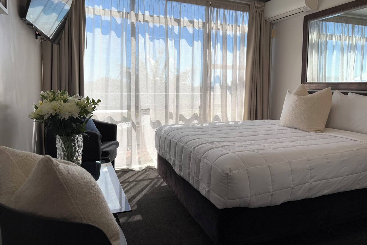 Una habitación de hotel con cama, una silla, una mesa y una ventana con cortinas.
