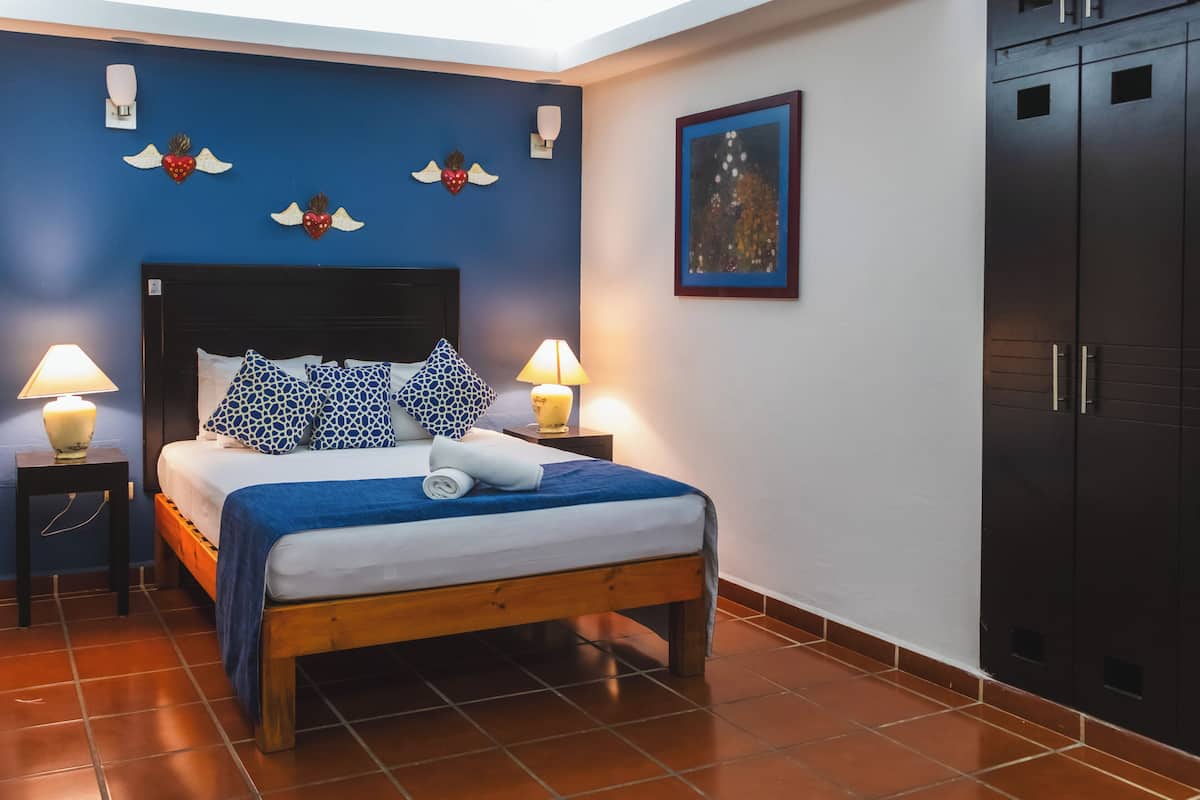 A bedroom with a bed, two bedside lamps, a blue wall with decorative wall art, and a wardrobe.