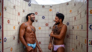 Dos hombres en una ducha con paredes de azulejos y diseños florales.
