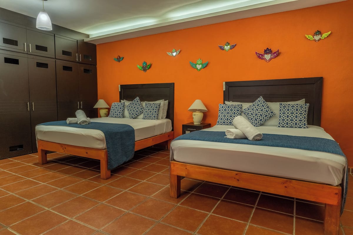 A hotel room with two beds, each with a wooden frame and white bedding. There are two bedside tables with lamps and decorative wall art above the beds.