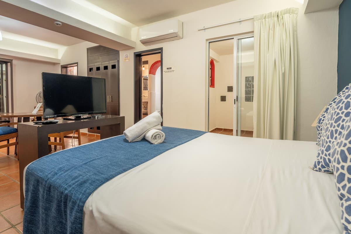 A hotel room with a bed, a desk with a television, a bathroom with a shower, and a dining area.