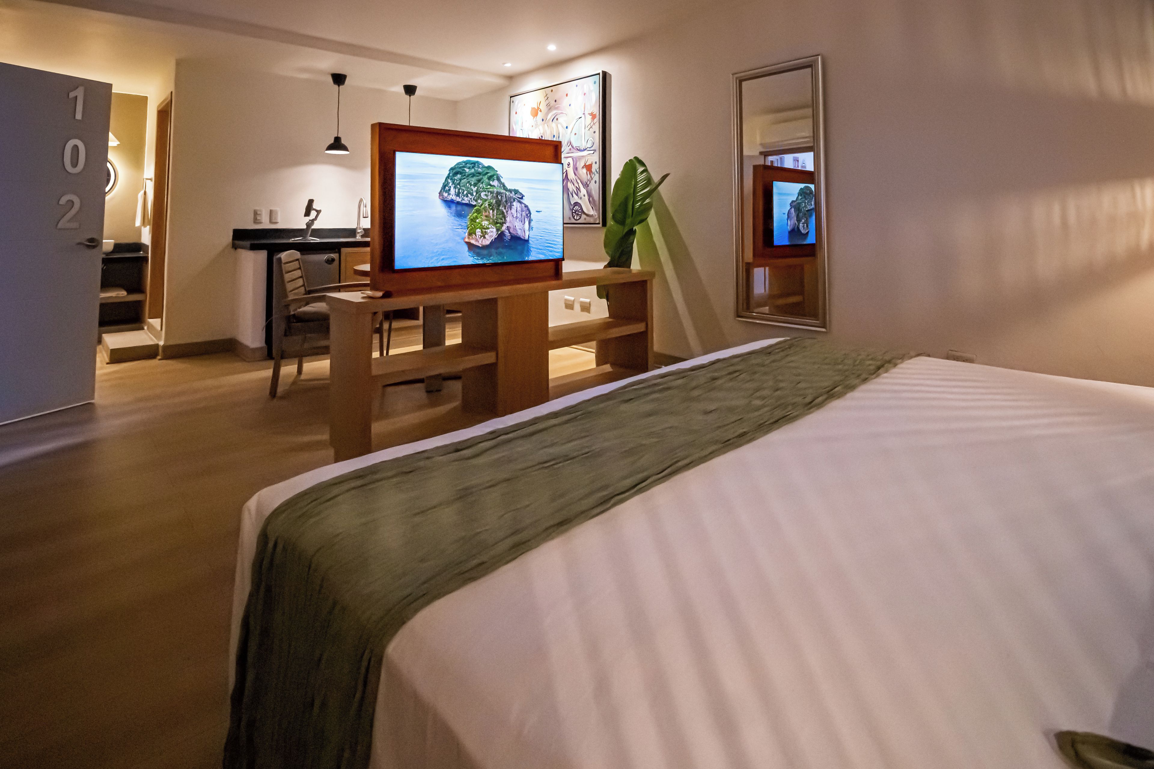 Et hotelværelse med seng, skrivebord, stol, fjernsyn og et spejl.