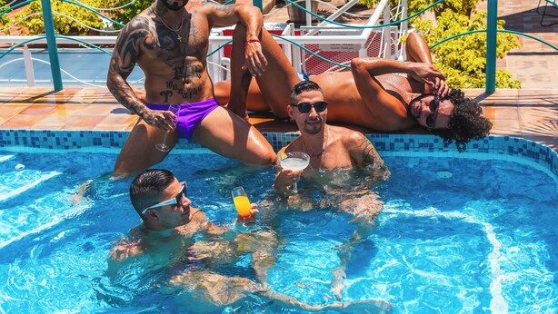 Una piscina con gente relajándose y sosteniendo bebidas.