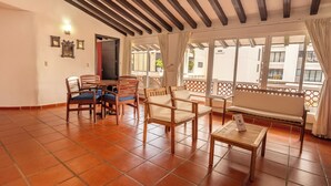 Una habitación con suelo de baldosas, muebles de madera, un balcón con vistas y una puerta que da al exterior.