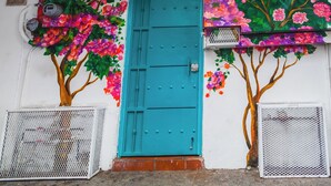 Un edificio con una puerta turquesa, un balcón con barandilla decorativa y una pared adornada con murales florales coloridos.