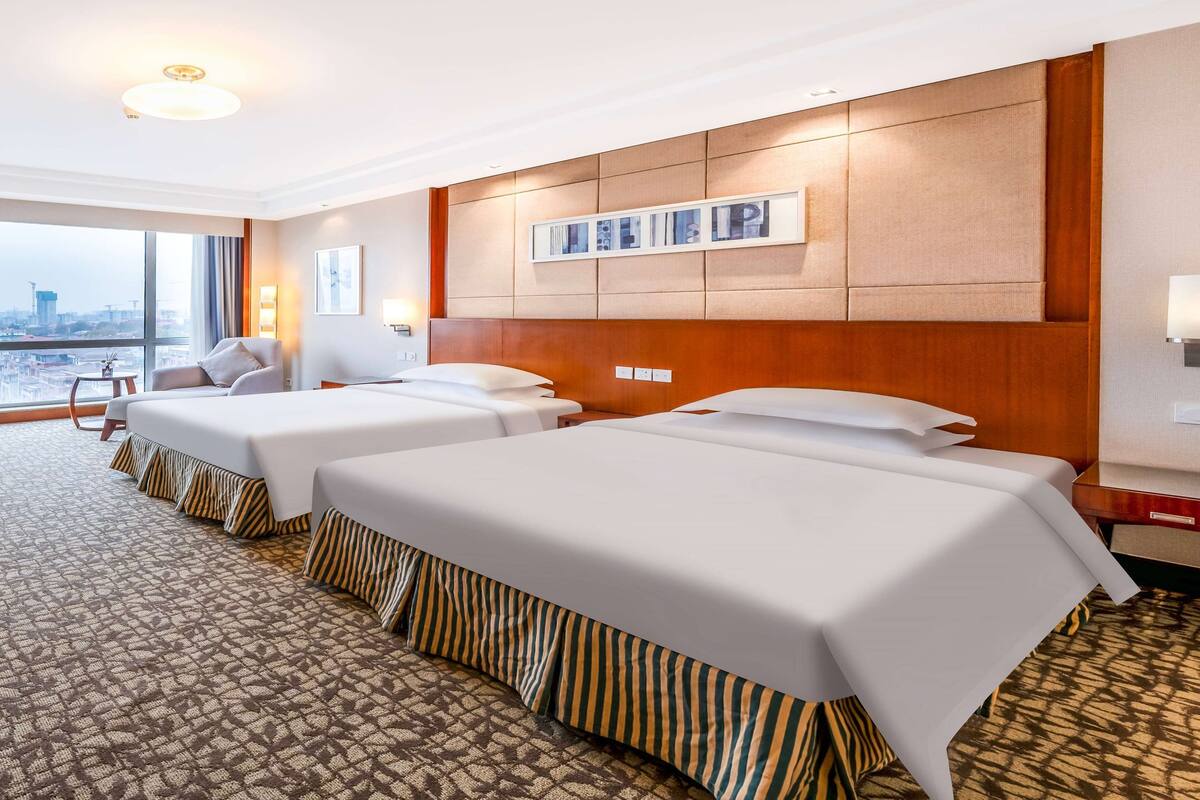 Habitación de hotel con dos camas, un ventanal grande con vistas a la ciudad y una alfombra estampada.