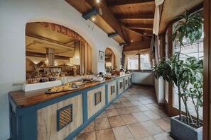 A long buffet counter with a variety of food items and a large potted plant on the right. - LUMA Stubai Aparthotel (Neustift Im Stubaital)