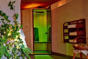 A room with a wooden door, a green-lit interior, a shelf with folded towels, and a basket of fruit. - LUMA Stubai Aparthotel (Neustift Im Stubaital)
