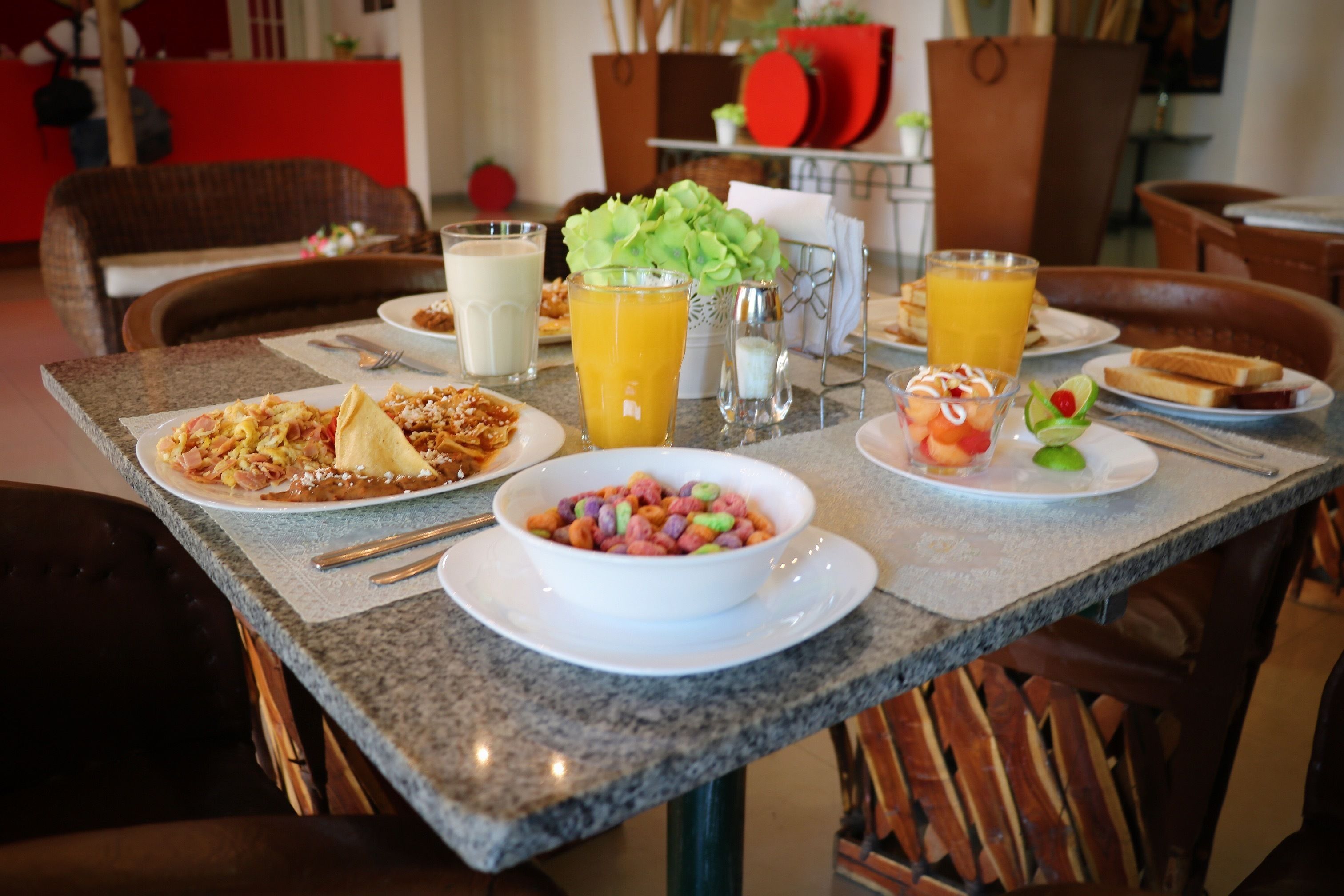 A breakfast table with plates of food, a bowl of cereal, and glasses of orange juice.