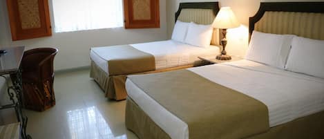 A hotel room with two single beds, a desk with a chair, and a lamp.