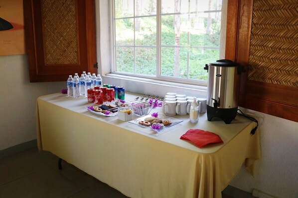 A table with water bottles, snacks, and a coffee maker, set against a window with a view of greenery. - Zar Colima (Cuauhtémoc)