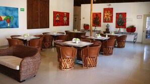 A restaurant with wicker furniture, red and blue paintings, and a wooden door. - Zar Colima (Cuauhtémoc)