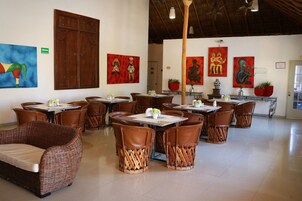 Un restaurante con mobiliario de mimbre, pinturas rojas y azules, y una puerta de madera.