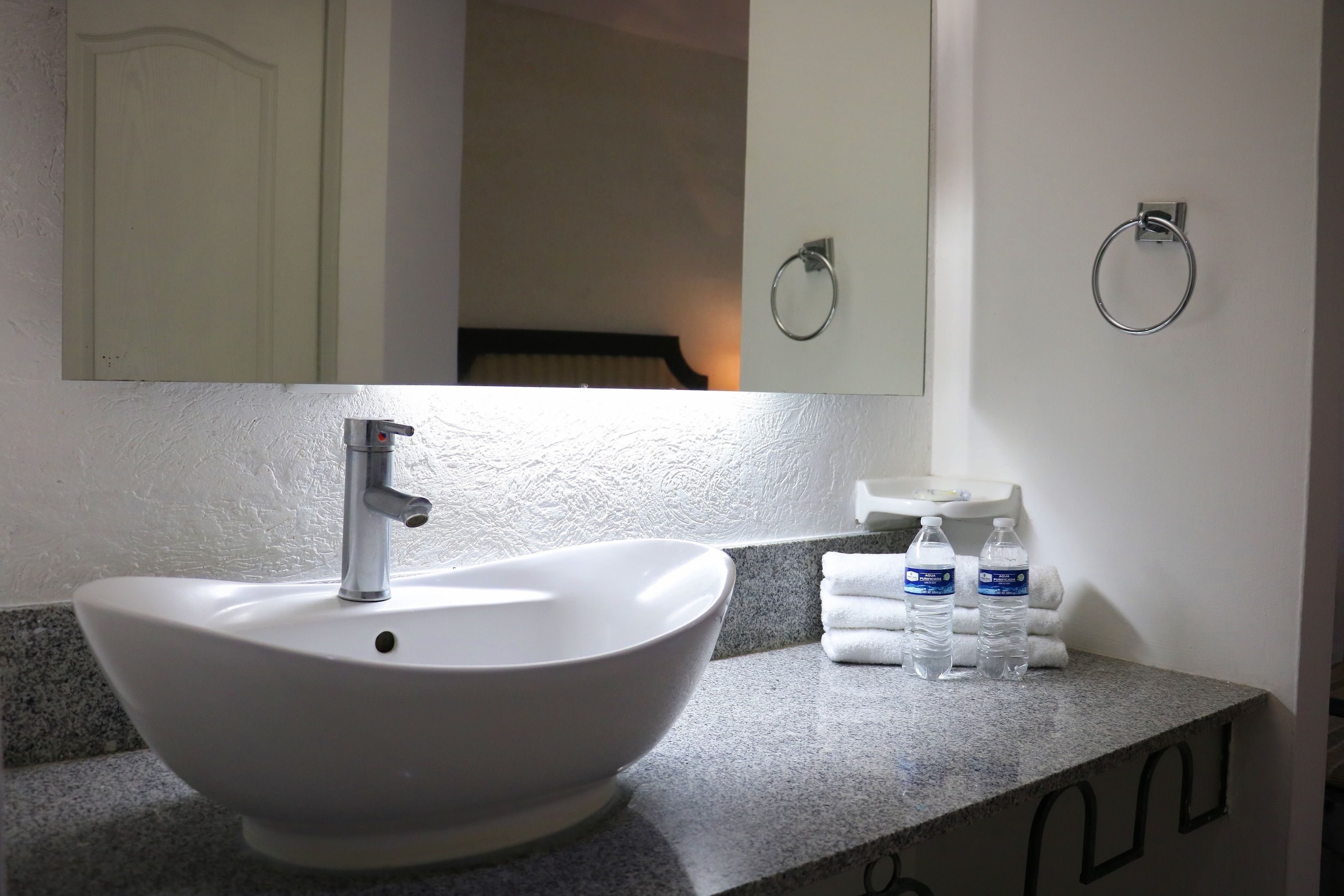 Une salle de bain avec un lavabo blanc, un miroir et deux bouteilles d’eau posées sur le comptoir.