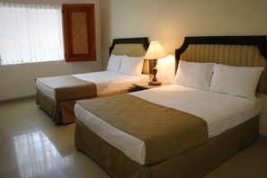 A hotel room with two beds, a nightstand, a lamp, and a window with blinds.