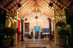 Un hall con techo de paja, candelabro y plantas en macetas.