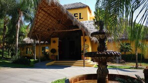 A hotel entrance with a thatched roof, a fountain, and palm trees. - Zar Colima (Cuauhtémoc)