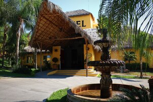 Una entrada de hotel con techo de paja, una fuente y palmeras.