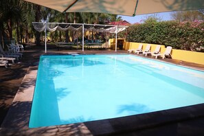 A rectangular swimming pool with a clear blue water surface, surrounded by white lounge chairs and a covered seating area with a white canopy.