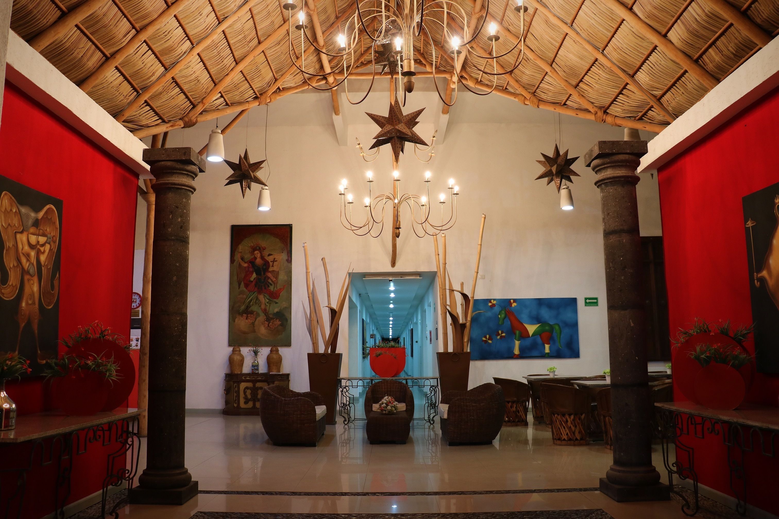 A lobby with a high ceiling, wooden beams, and a star-shaped chandelier. There are two large columns and wicker chairs in the center.