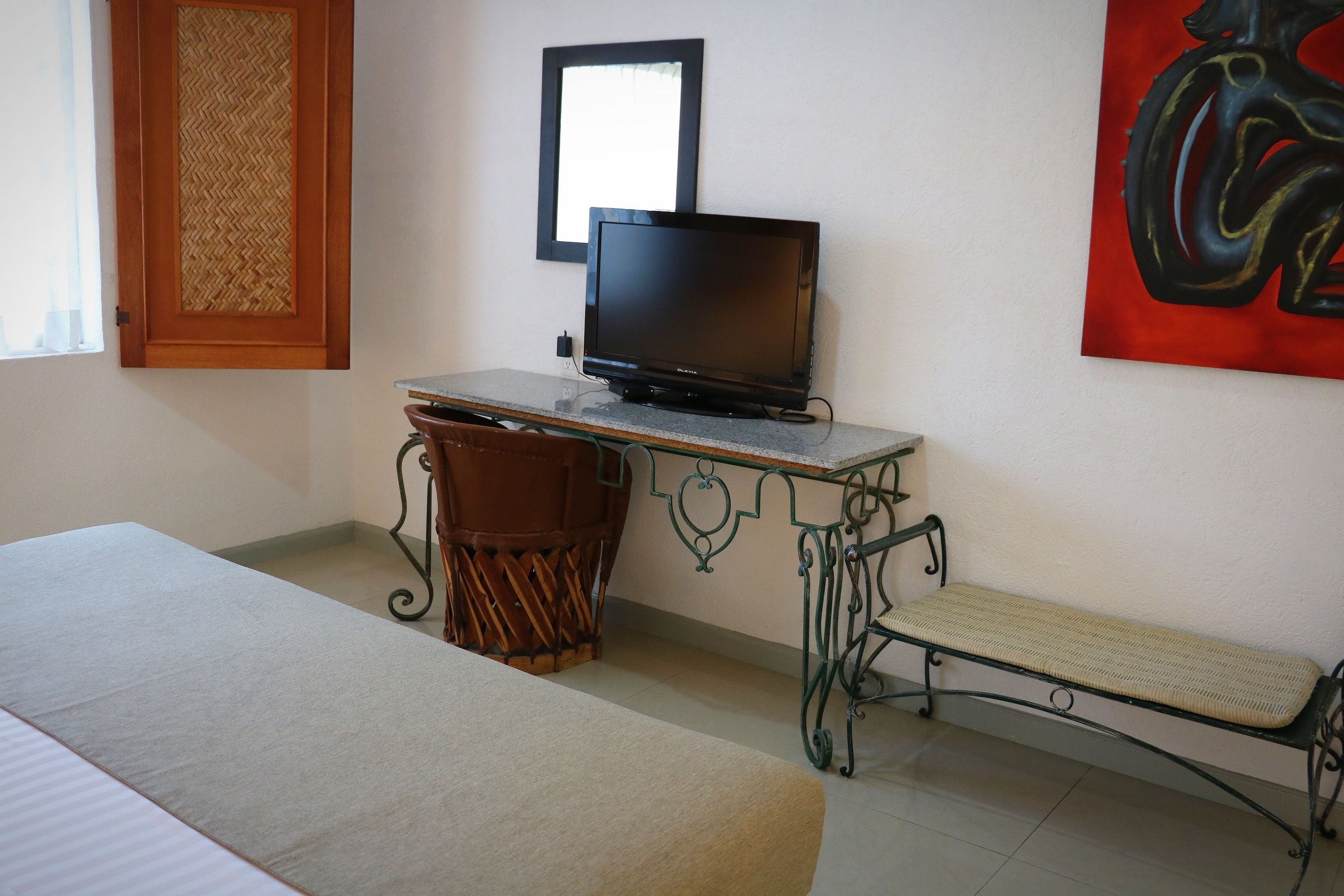 Ein Zimmer mit einem Bett, einem Schreibtisch mit Computer, einem Stuhl, einer Bank und einem Bild an der Wand.