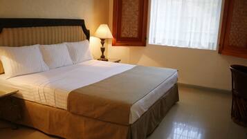 Una cama bien hecha con cabecera de madera, lámpara de noche y ventana con un panel decorativo.