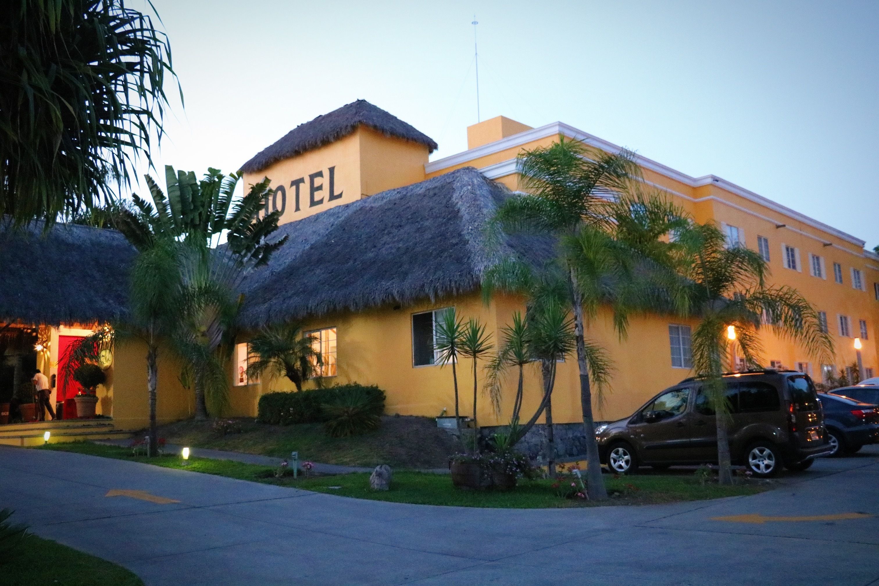 Ein Hotel mit einem Strohdach, Palmen und einem gepflegten Rasen.