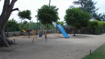 Kids can play on swings and a slide in this outdoor playground surrounded by trees.