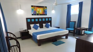 Quarto de hotel com cama grande, escrivaninha, cadeira, lixeira e um quadro na parede.