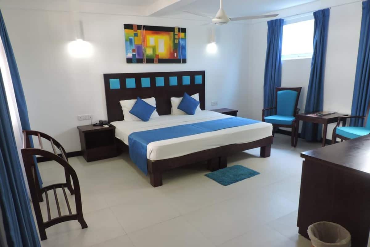 A hotel room with a large bed, a desk, a chair, a waste bin, and a painting on the wall.