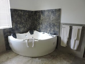 A modern bathroom with a freestanding bathtub, a large mirror, and a towel rack with towels. - Pigeon Island Beach Resort (Nilaveli)