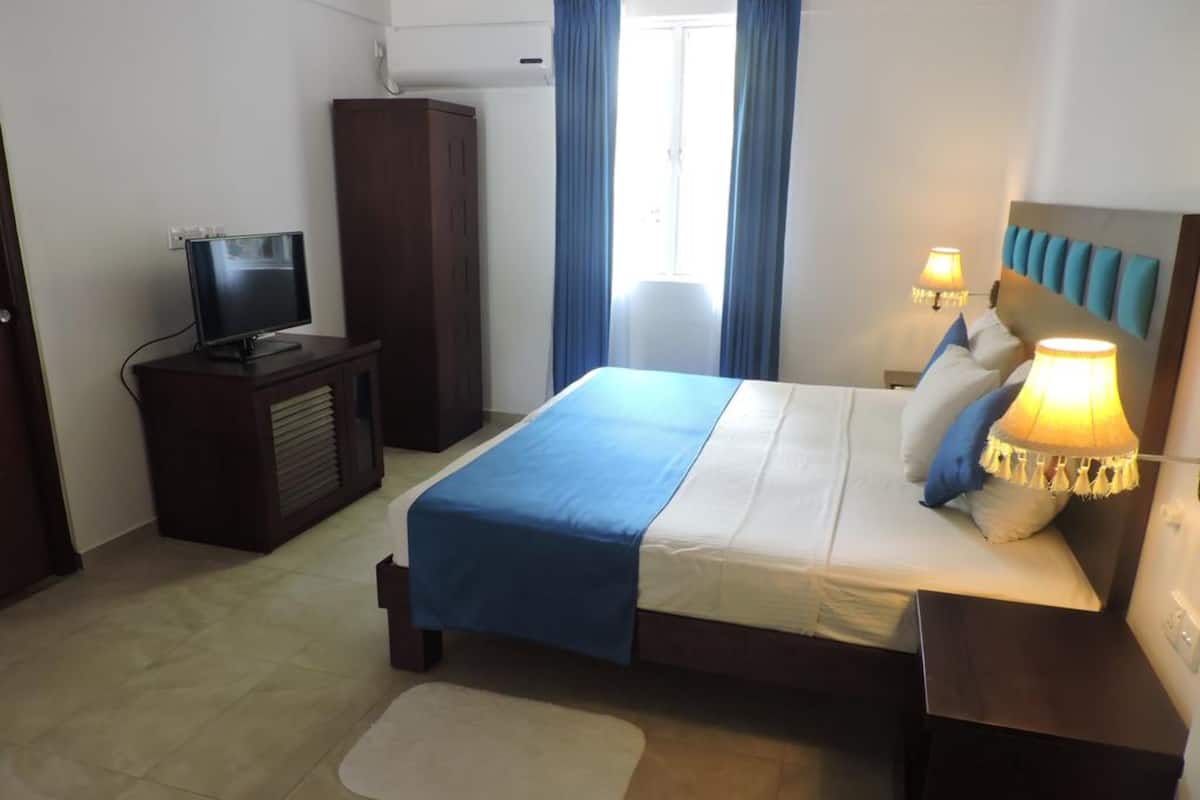 A hotel room with a bed, a TV, a wardrobe, and a desk with a lamp.