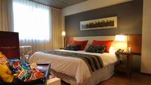 Een hotelkamer met een net opgemaakt bed, een nachtkastje met een lamp, een telefoon en een minibar.