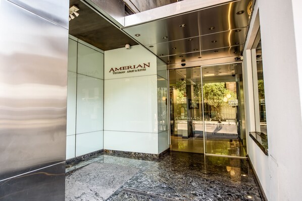 Une entrée moderne avec une porte en verre et une enseigne indiquant « AMERICAN TUCUMAN APART & SUITES ».
