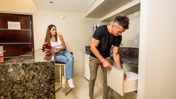 A modern kitchen with a granite countertop, a woman reading a magazine, and a man leaning over a counter.