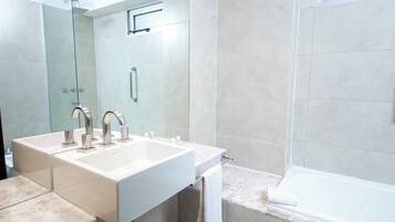 A modern bathroom with two sinks, a glass shower enclosure, and a bathtub.
