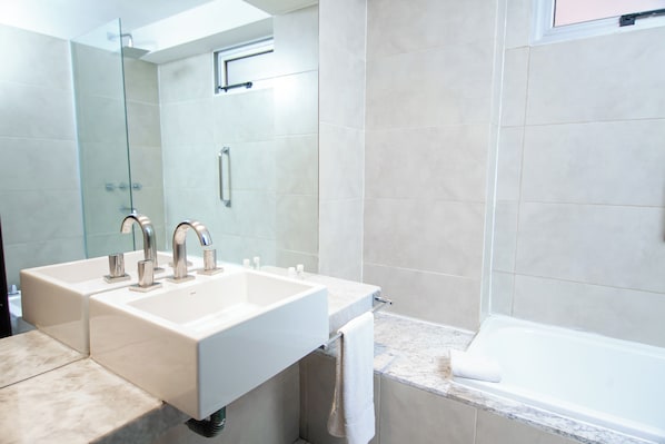 A modern bathroom with two sinks, a glass shower enclosure, and a bathtub.