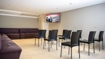 Un salón de conferencias con una pantalla grande, un sofá y varias sillas dispuestas alrededor de una mesa.