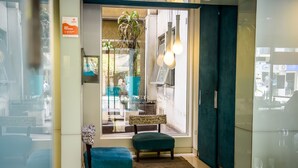 Een hotellobby met een glazen scheiding, teal bekleding en een potplant.