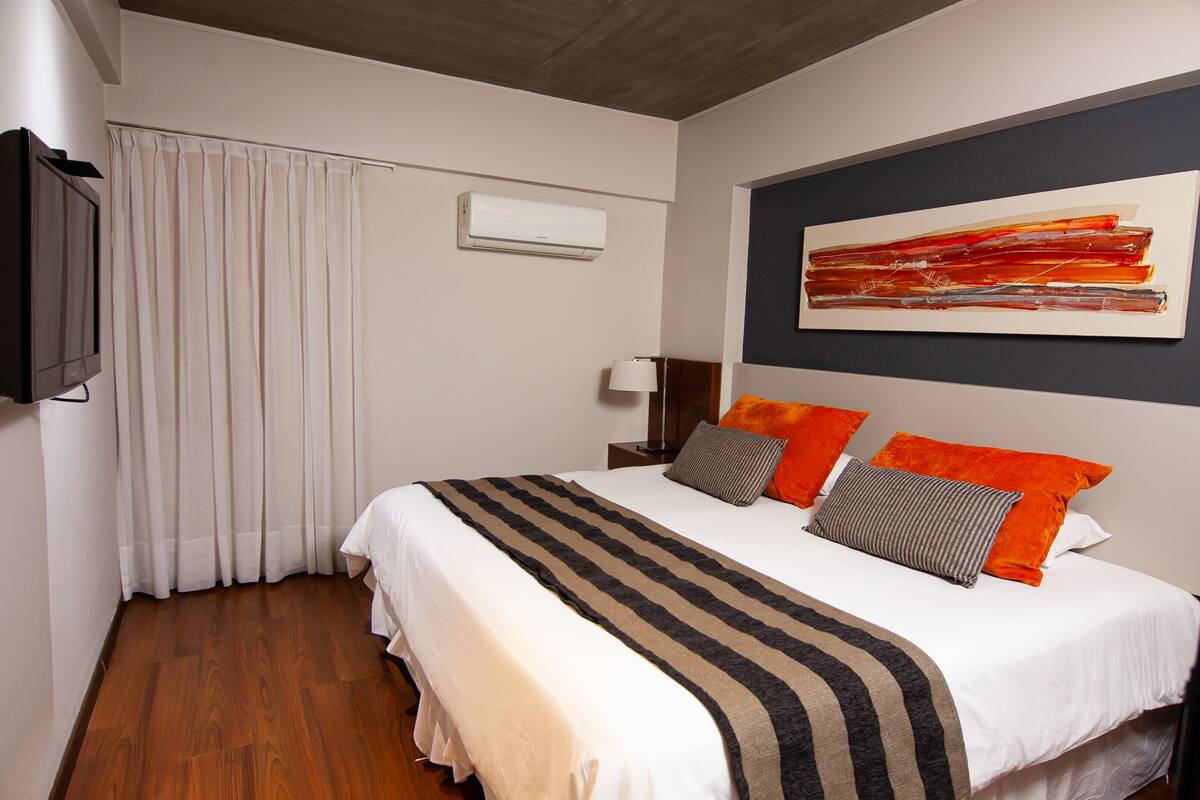 Habitación de hotel con una cama grande, un televisor de pantalla plana, un ventilador de techo y una ventana con cortinas.