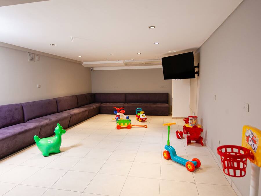 Una sala de estar con un sofá modular, juguetes infantiles, un televisor montado en la pared y un aro de baloncesto.