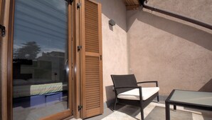 A room with a sliding glass door leading to a bed, a wicker chair with a cushion, and a small table. - Hotel De Rome (Rome)