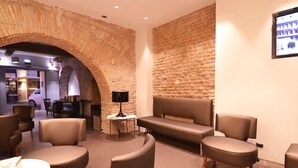 A modern interior with a stone archway, leather seating, and a small table with a lamp. - Hotel De Rome (Rome)