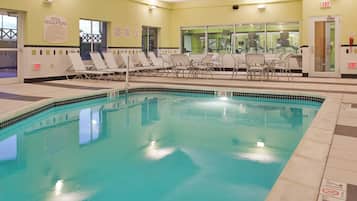 Una piscina interior con agua cristalina, sillones de descanso y una zona junto a la piscina con mesa y sillas.