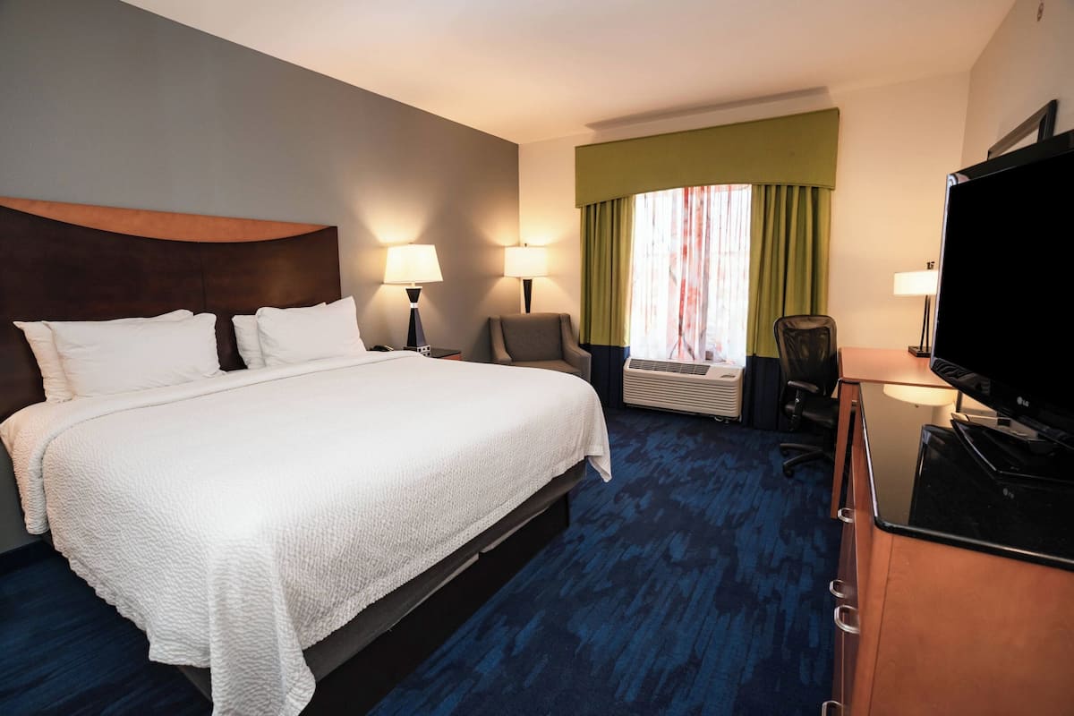A hotel room with a large bed, two bedside lamps, a desk with a television, and a window with curtains.
