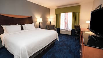 A hotel room with a large bed, two bedside lamps, a desk with a television, and a window with curtains.