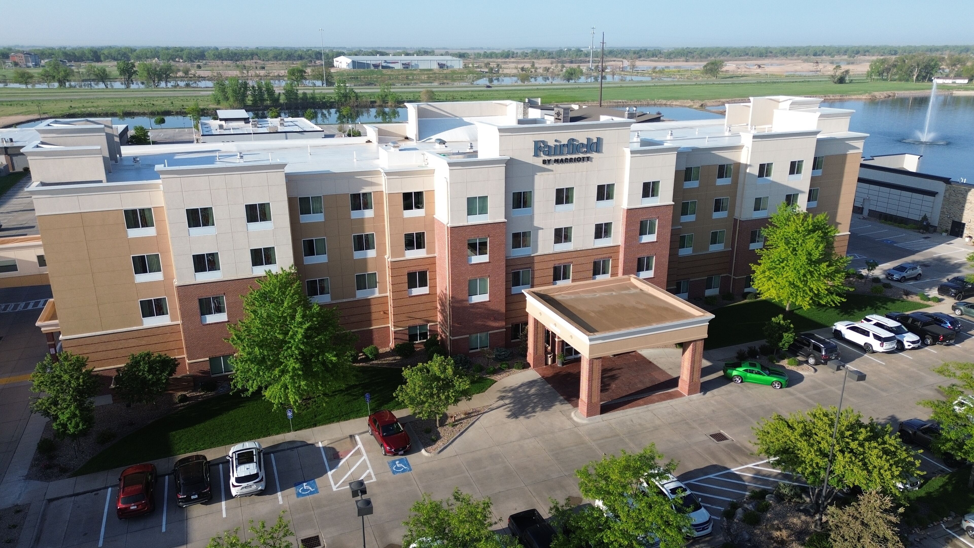 A multi-story hotel with a flat roof, parking lot, and a view of a lake.