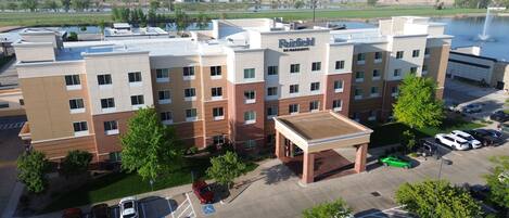 A multi-story hotel with a flat roof, parking lot, and a view of a lake.