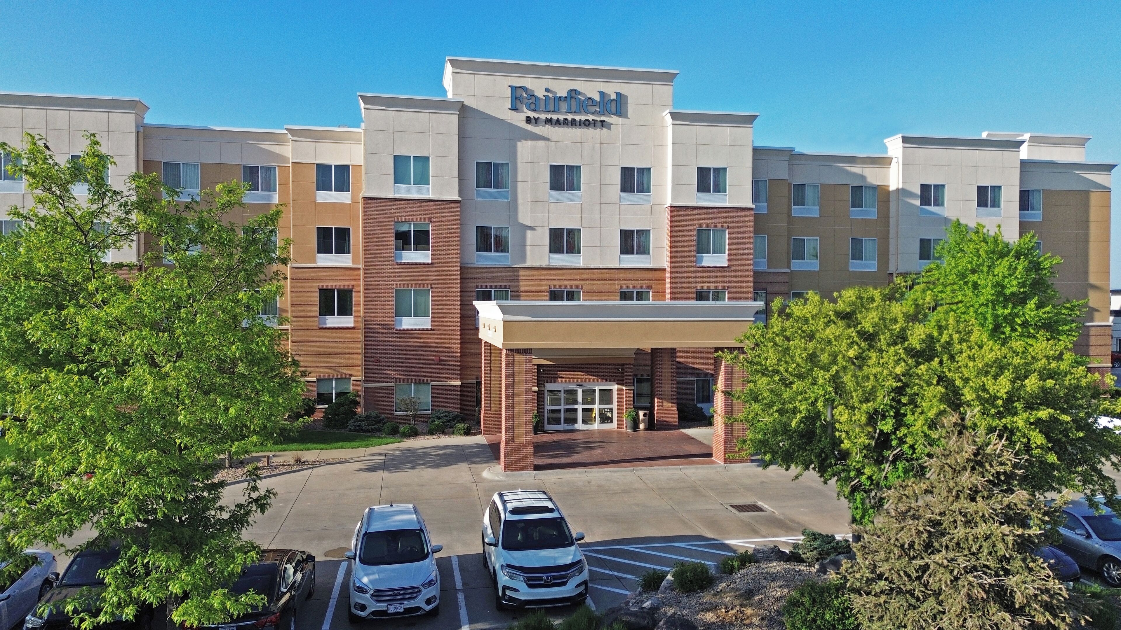 A Fairfield by Marriott hotel with a modern brick facade, a covered entrance, and a parking lot with several cars.